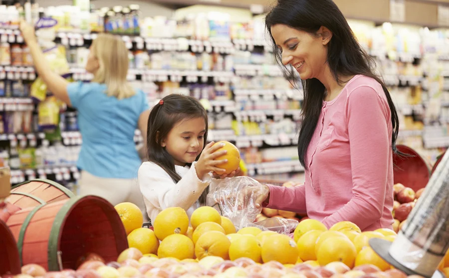 Mother And Daughter At Fruit Counter In Supermarket Putting Fruit Into A Bag