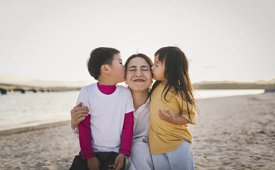 Kids kissing mother in the beach at dusk